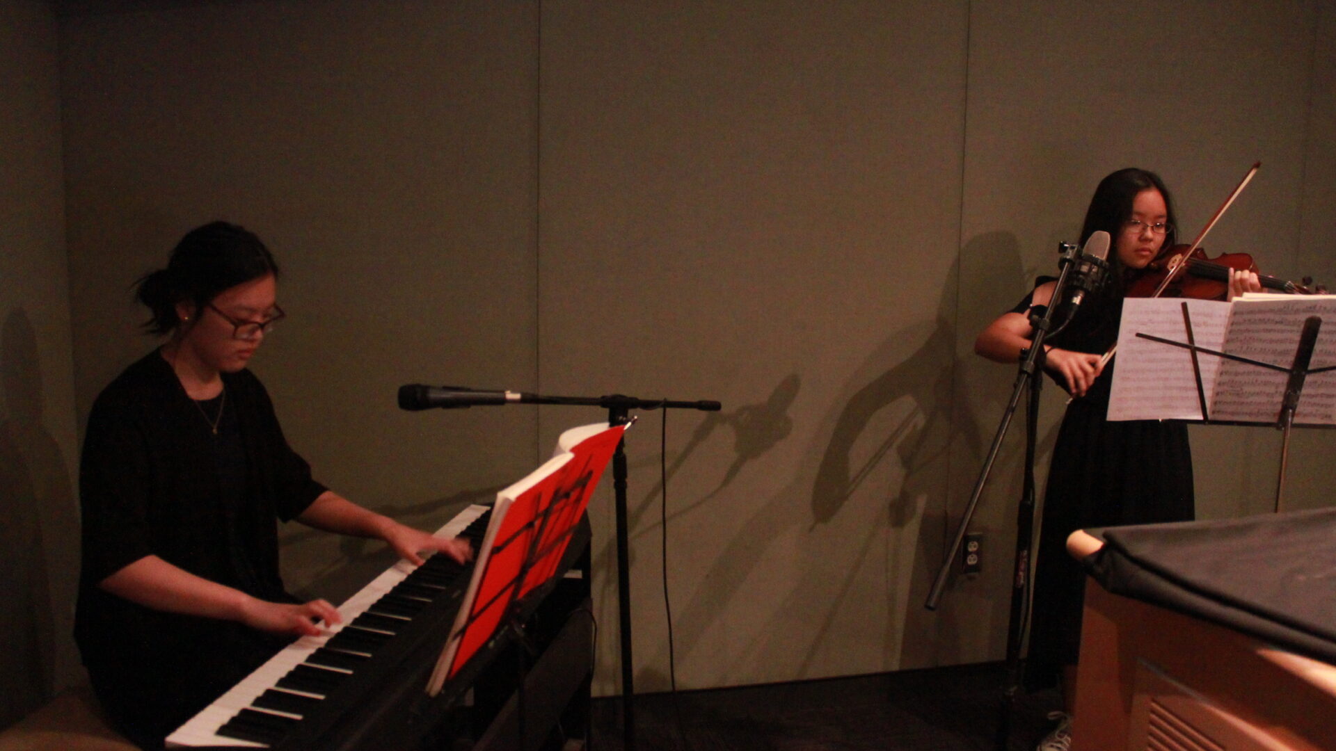 Two youth performing on piano keyboard and violin looking at sheet music on music stands in a radio studio