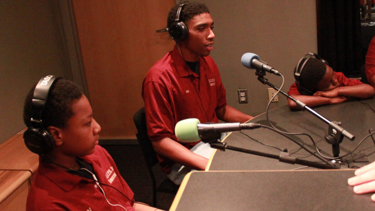 Three youth wearing headphones and speaking into microphones in a radio studio