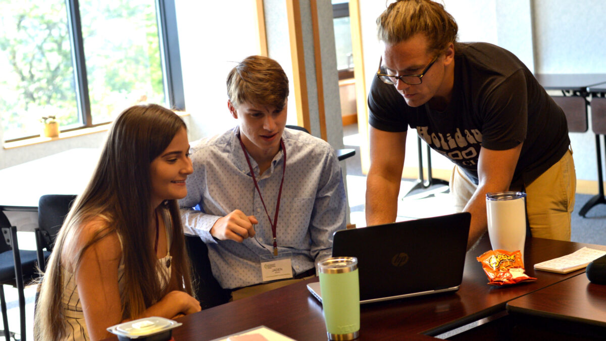 Two teens and an adult looking at a laptop on a wooden table