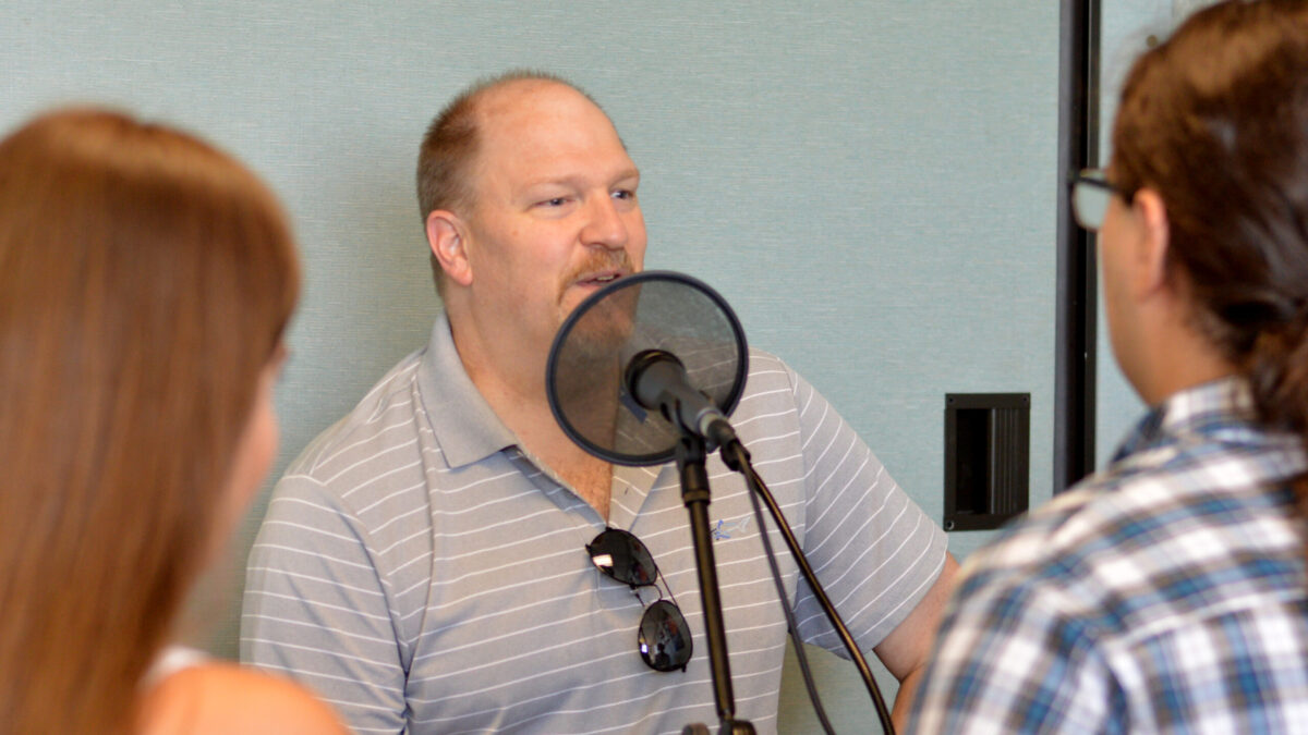 Two teens interviewing an adult speaking into a microphone with a pop filter