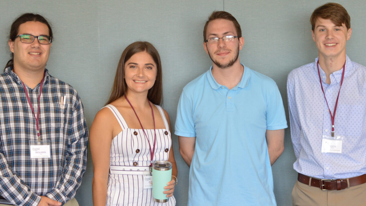 Four teens smiling and posing in profile in front of a blue-gray wall