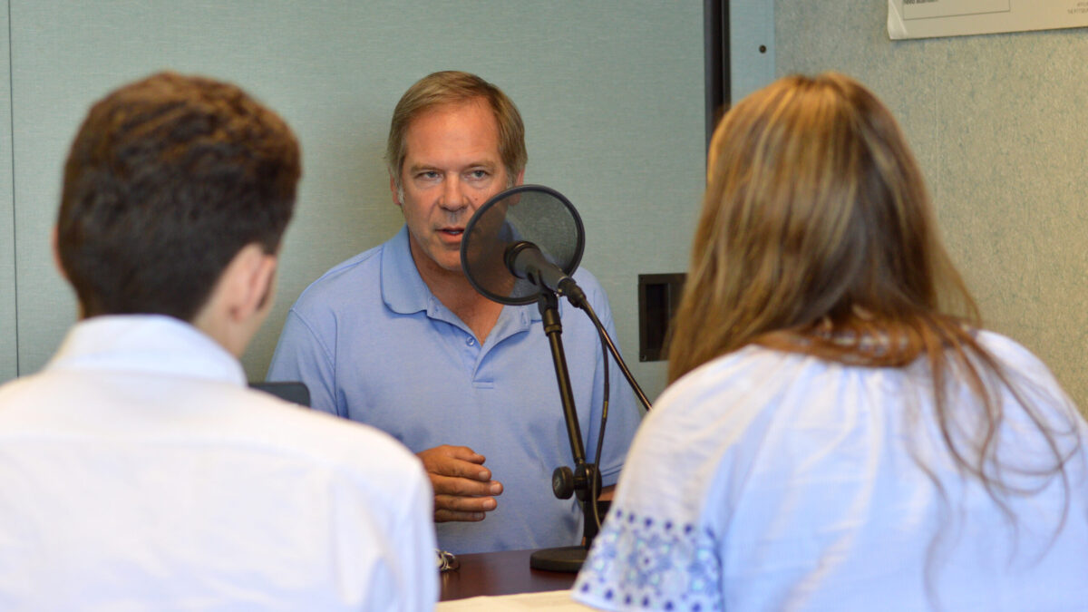 Two teens interviewing an adult speaking into a microphone