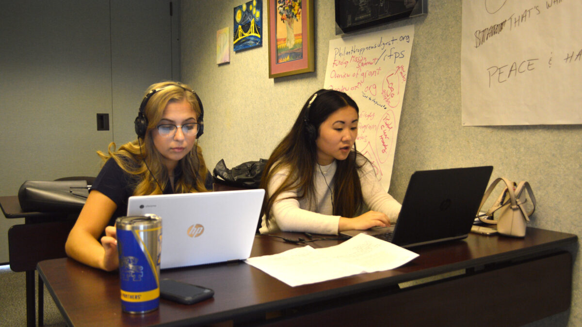 Two teens wearing headphones looking at laptop computers on a wooden table