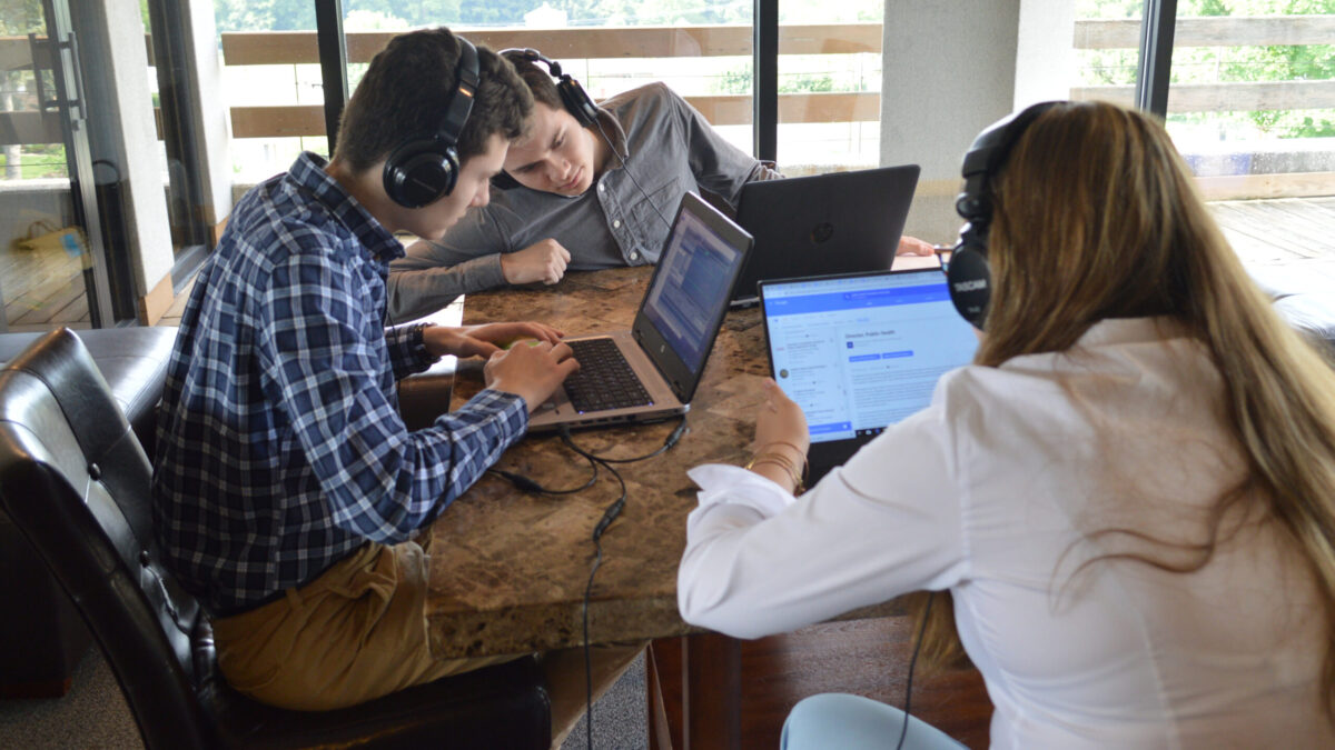 Three teens wearing headphones and looking at laptop computers on a marble table