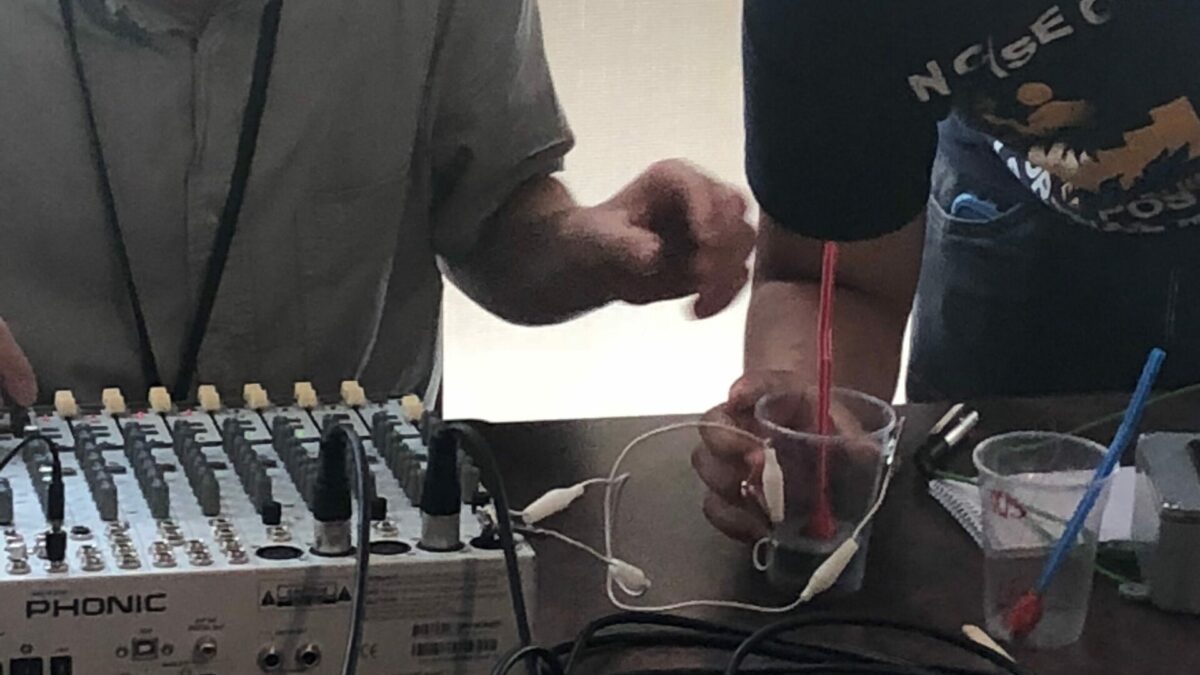 Adult and youth looking at a plastic cup connected to a mixing board