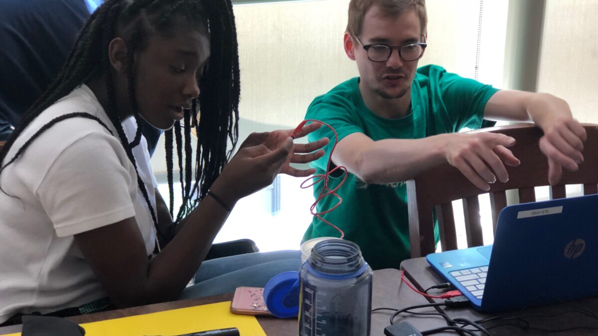 An adult gesturing with their hands and a teen looking at a blue laptop