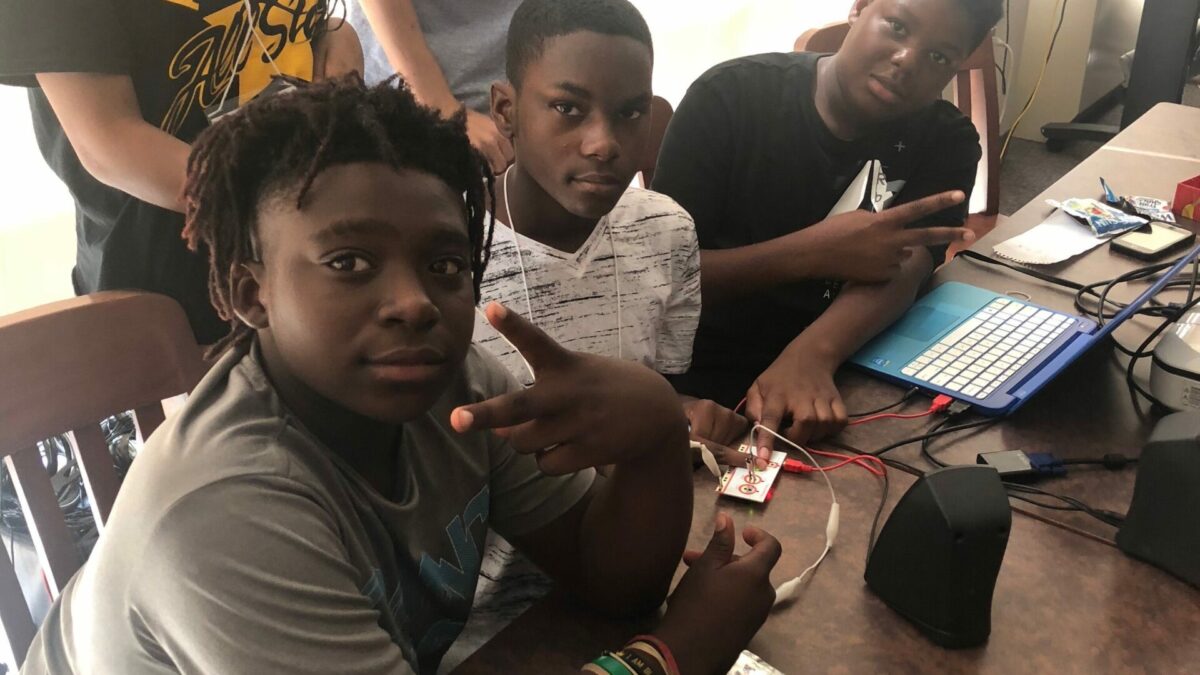 Two adults and three youths posing in front of a blue laptop on a blue table