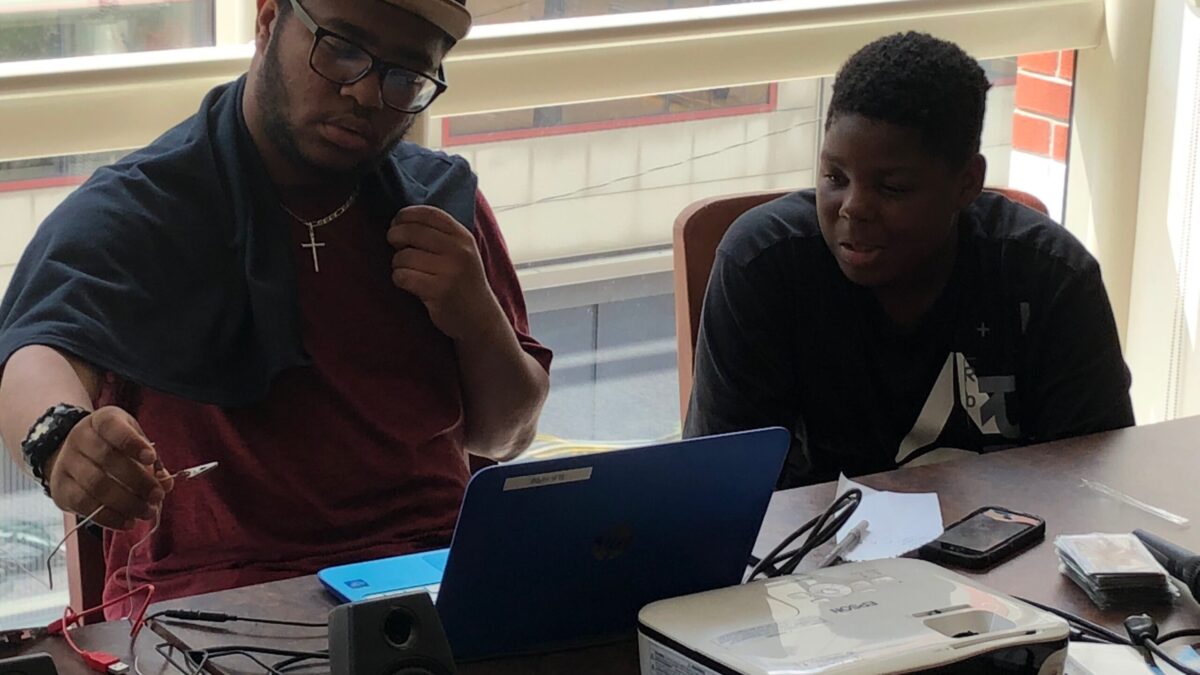 Two youth looking at a blue laptop in front of a projector on a brown table