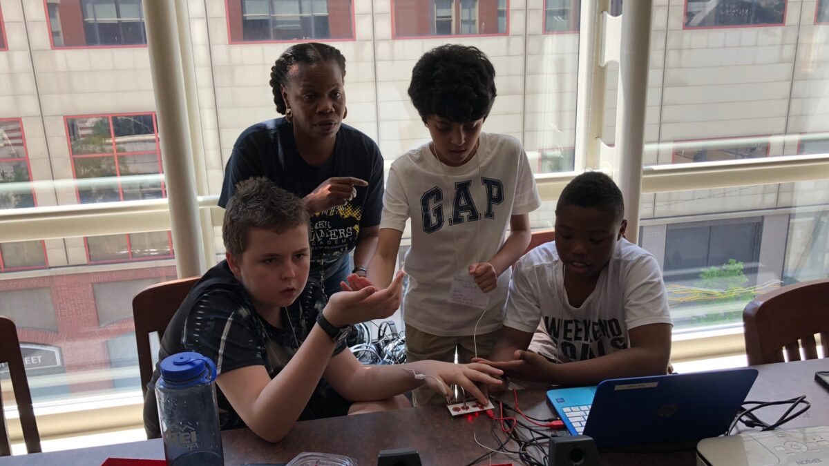 Three youth and an adult looking at a blue laptop on a brown table