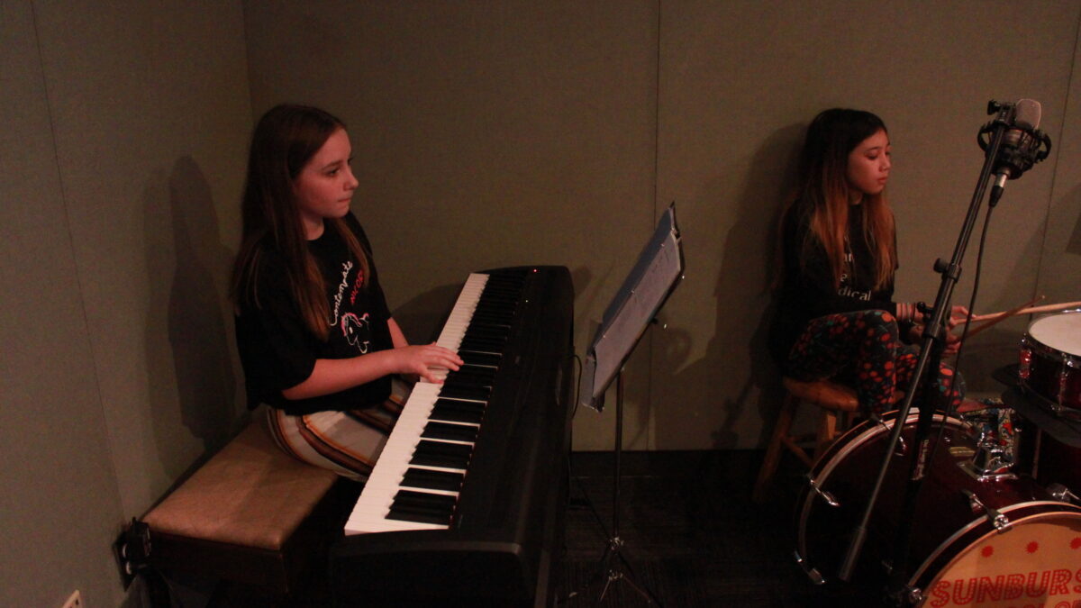 Two youth playing piano keyboard and drum set in a radio studio