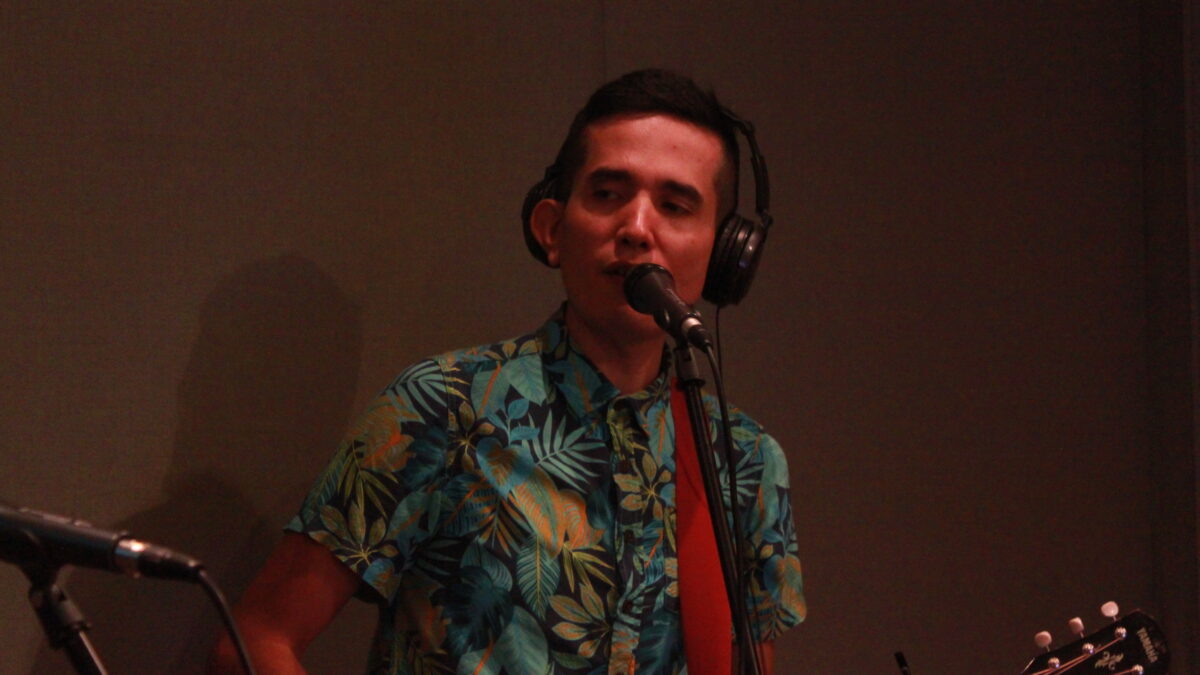 Adult wearing headphones playing guitar and singing into a microphone in a radio studio