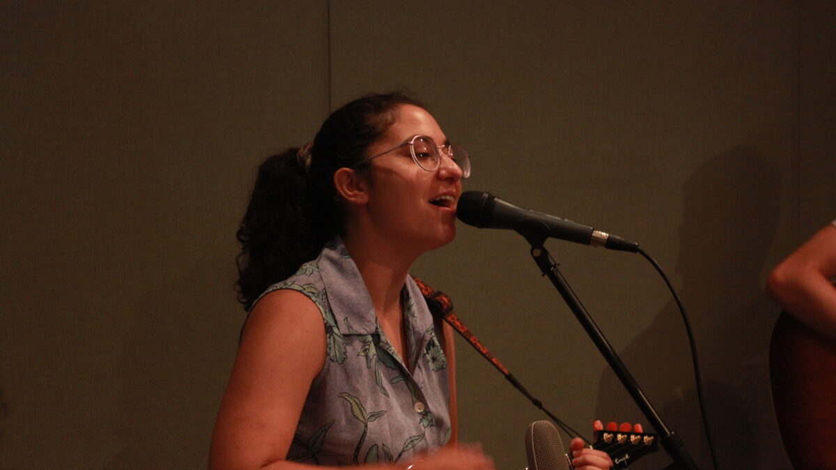 Adult singing into a microphone and playing a ukulele in a radio studio