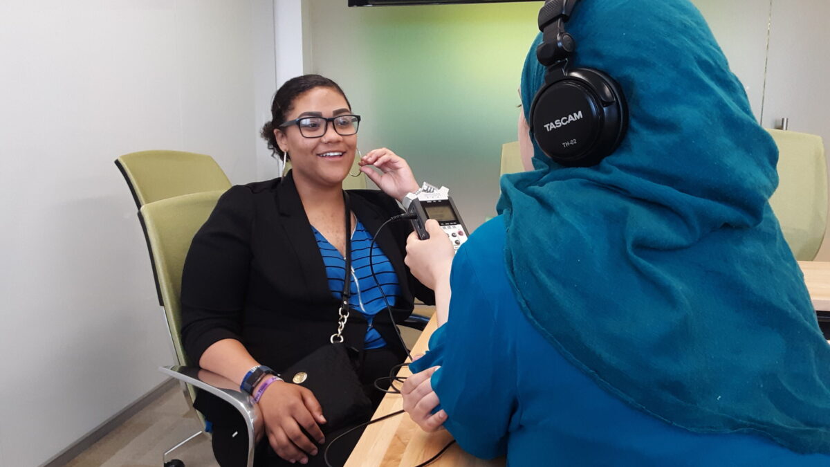 An individual wearing headphones interviewing an adult with a portable recorder