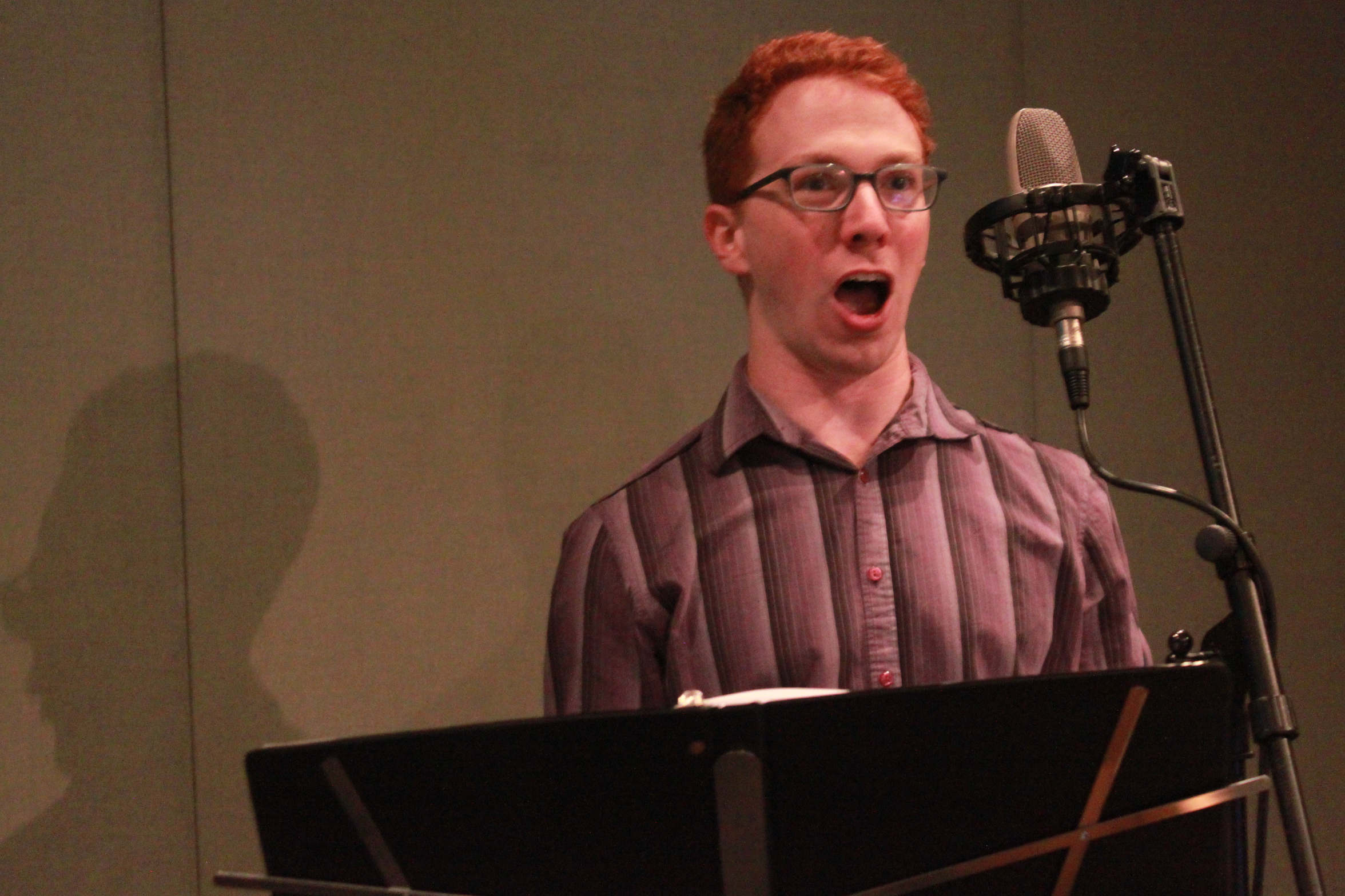 Adult singing into a microphone behind a music stand in a radio studio