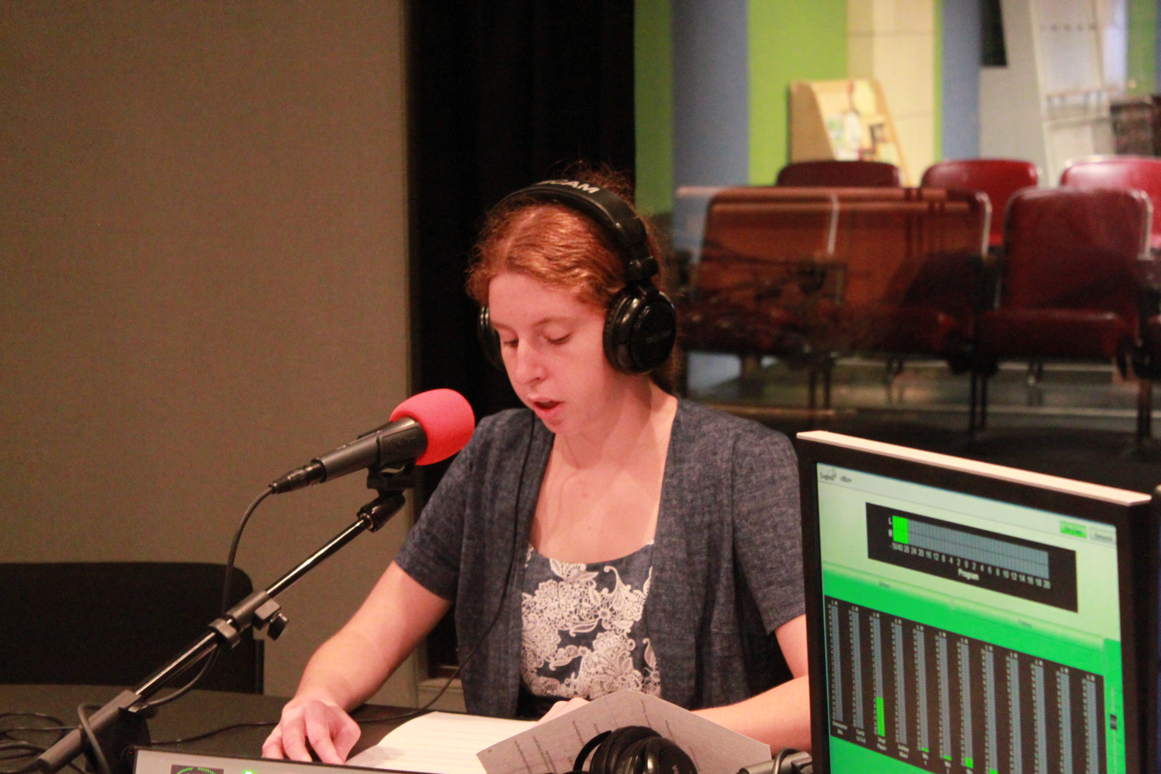 Teen wearing headphones and speaking into a microphone while looking down at pieces of paper in a radio studio
