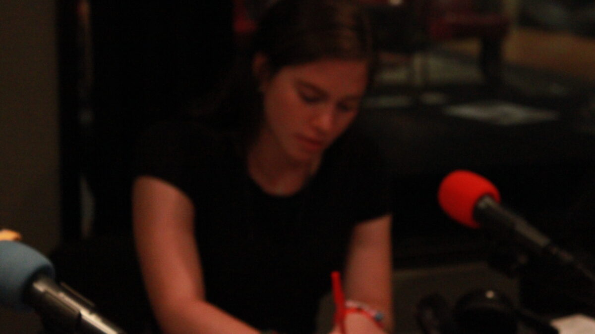 Young adult sitting behind a microphone writing on a piece of paper in a radio studio