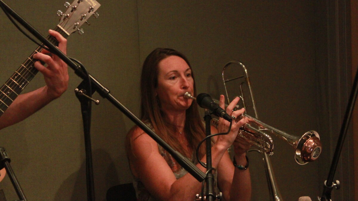 An adult playing a muted trumpet into a microphone in a radio studio
