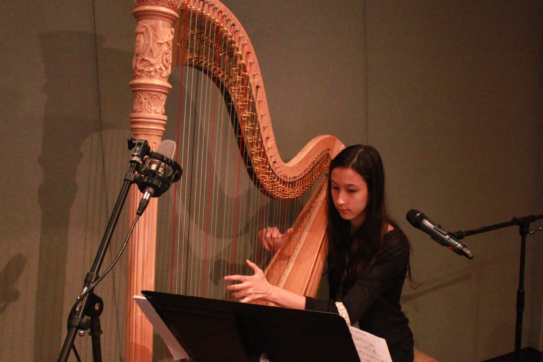 A youth playing harp and looking at sheet music on a music stand in a radio studio