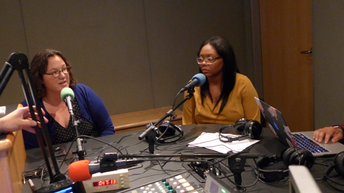 Two adults speaking into microphones in a radio studio