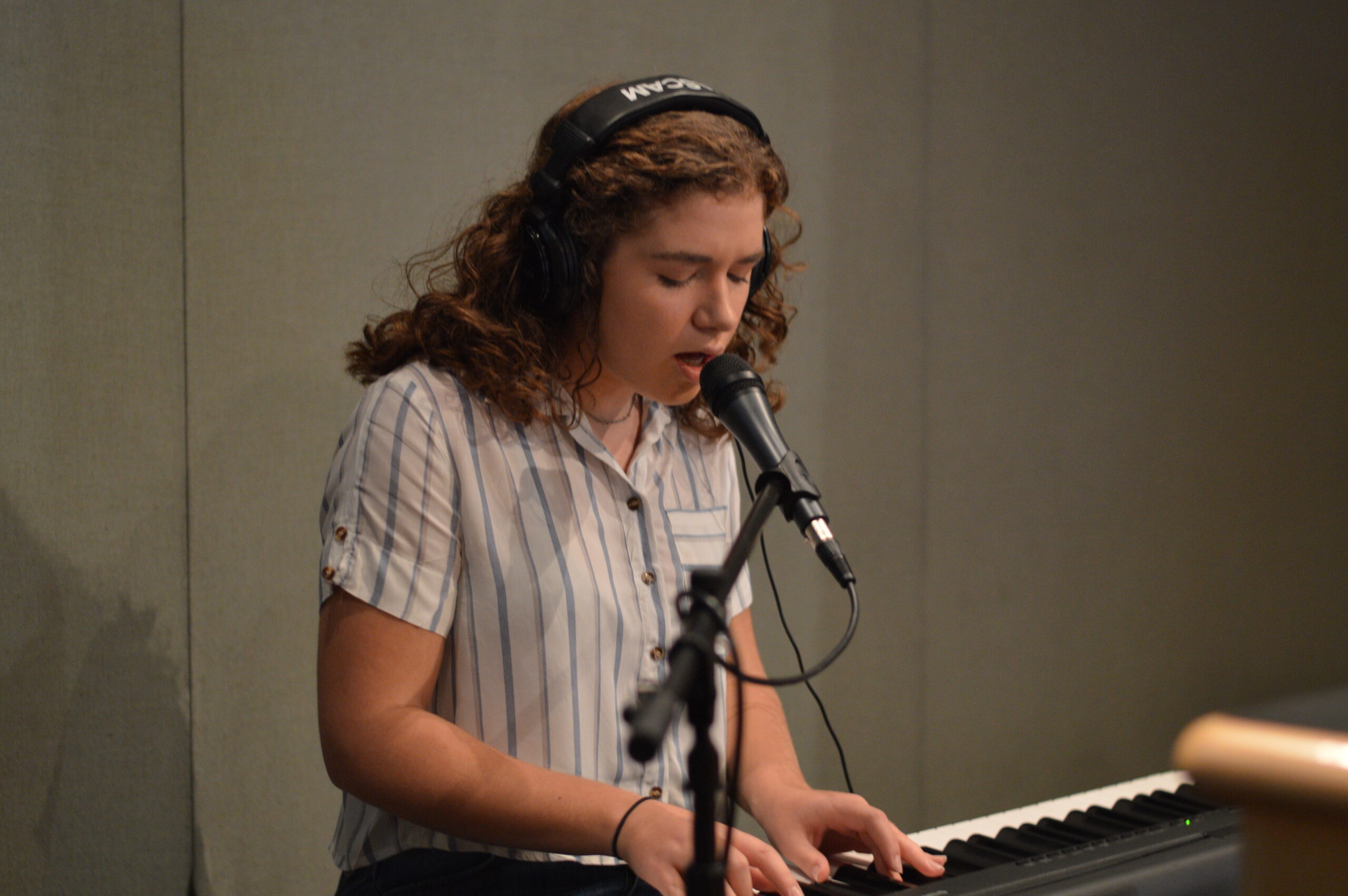 Teen wearing headphones and singing into a microphone while playing piano in a radio studio
