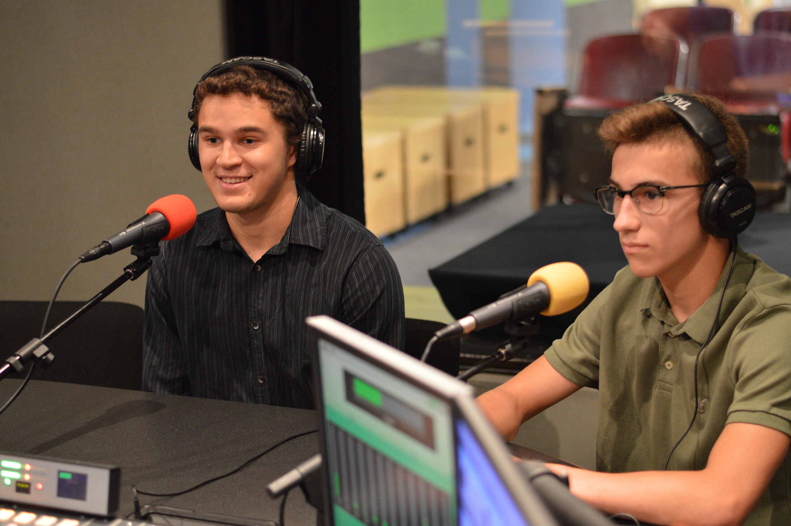 Two teens wearing headphones and speaking into microphones in a radio studio