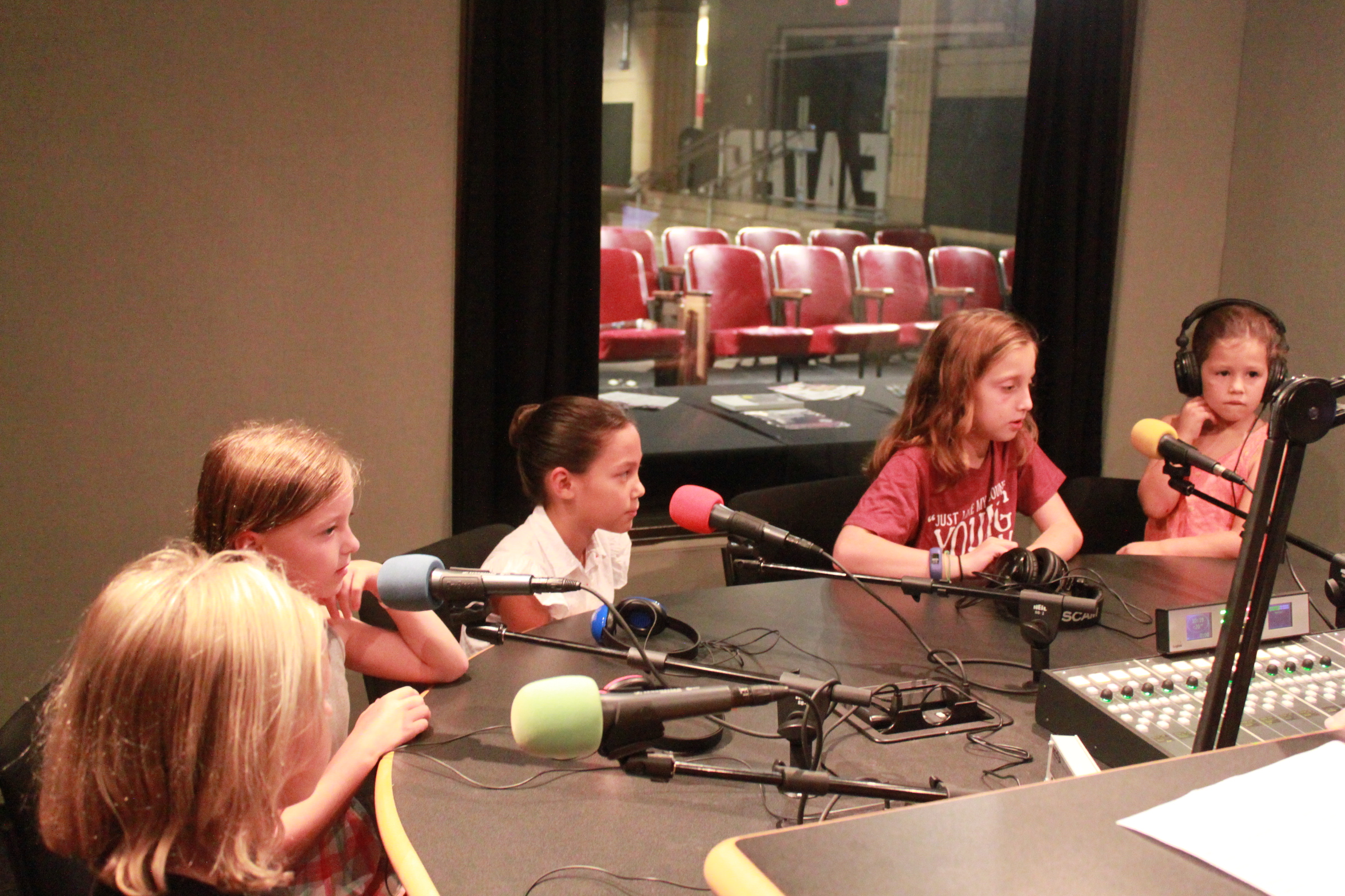 Five children speaking into microphones in a radio studio