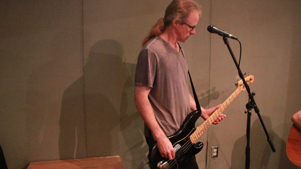 Adult playing bass in front of a microphone in a radio studio