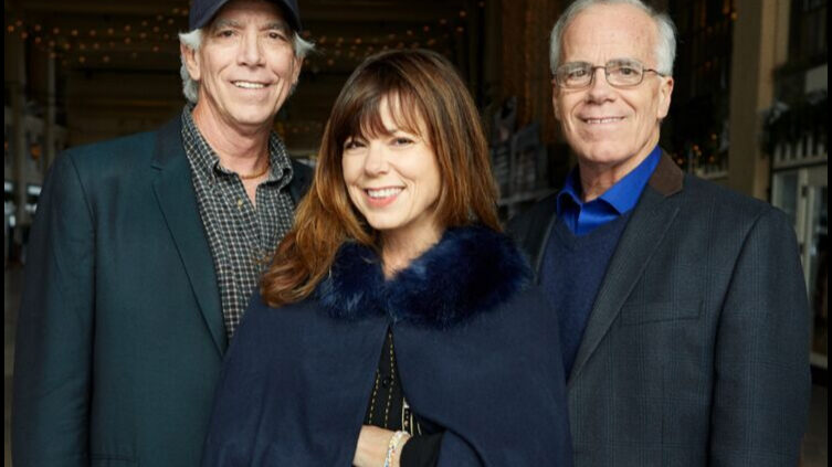 Three adults wearing dark blue outfits smiling and posing in profile
