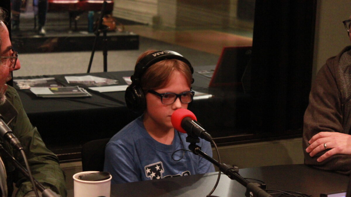 One youth wearing glasses and headphones speaking into a microphone in a radio studio