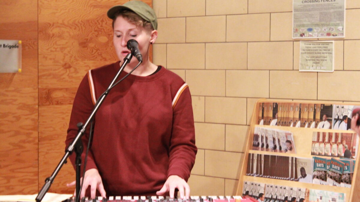 Adult playing piano keyboard and singing into a microphone outside a radio studio