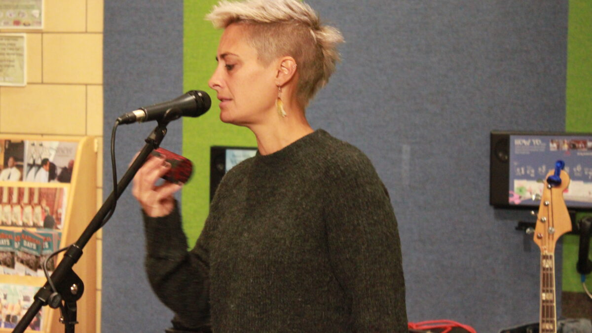 Adult playing a shaker and singing into a microphone