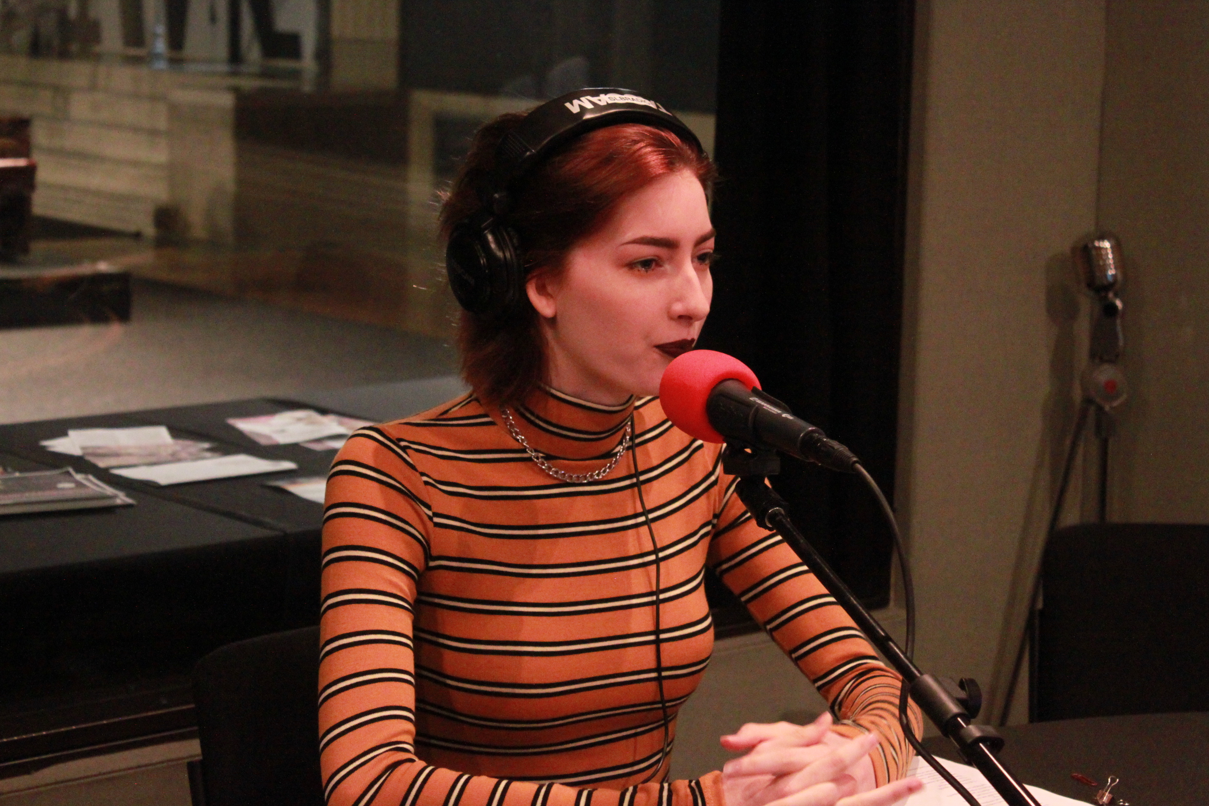 Young adult wearing headphones and sitting in front of a microphone in a radio studio