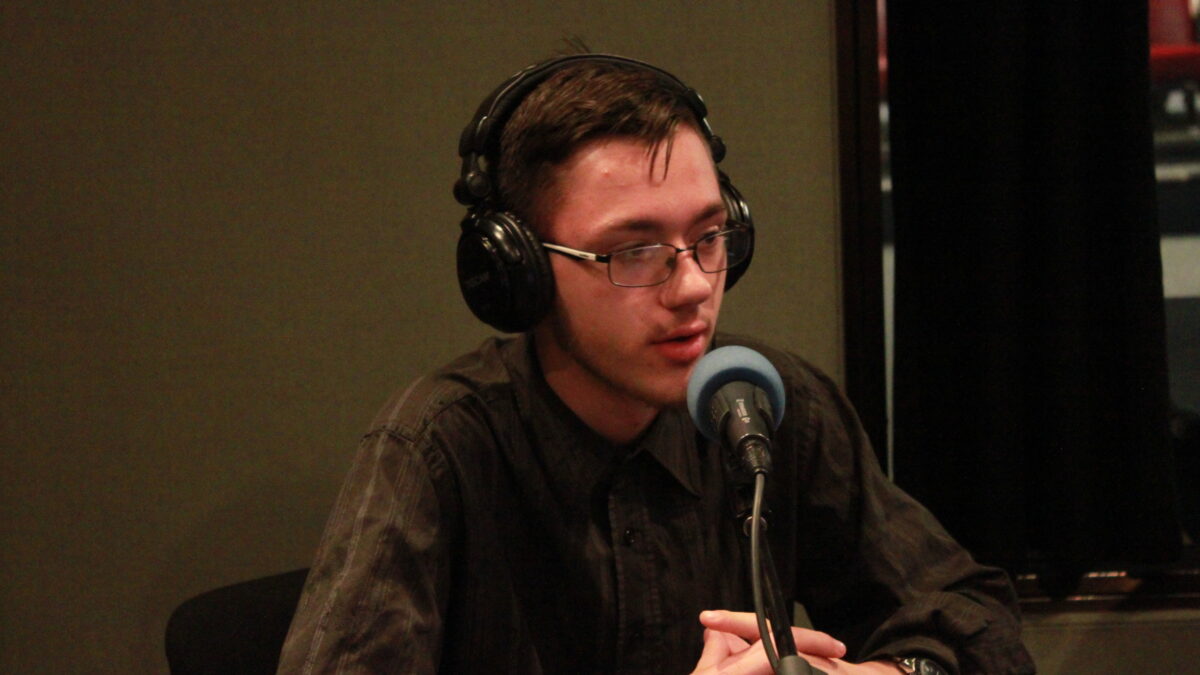 Teen wearing glasses and headphones speaking into a microphone in a radio studio