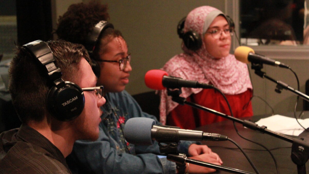 Three teens wearing headphones speaking into microphones in a radio studio
