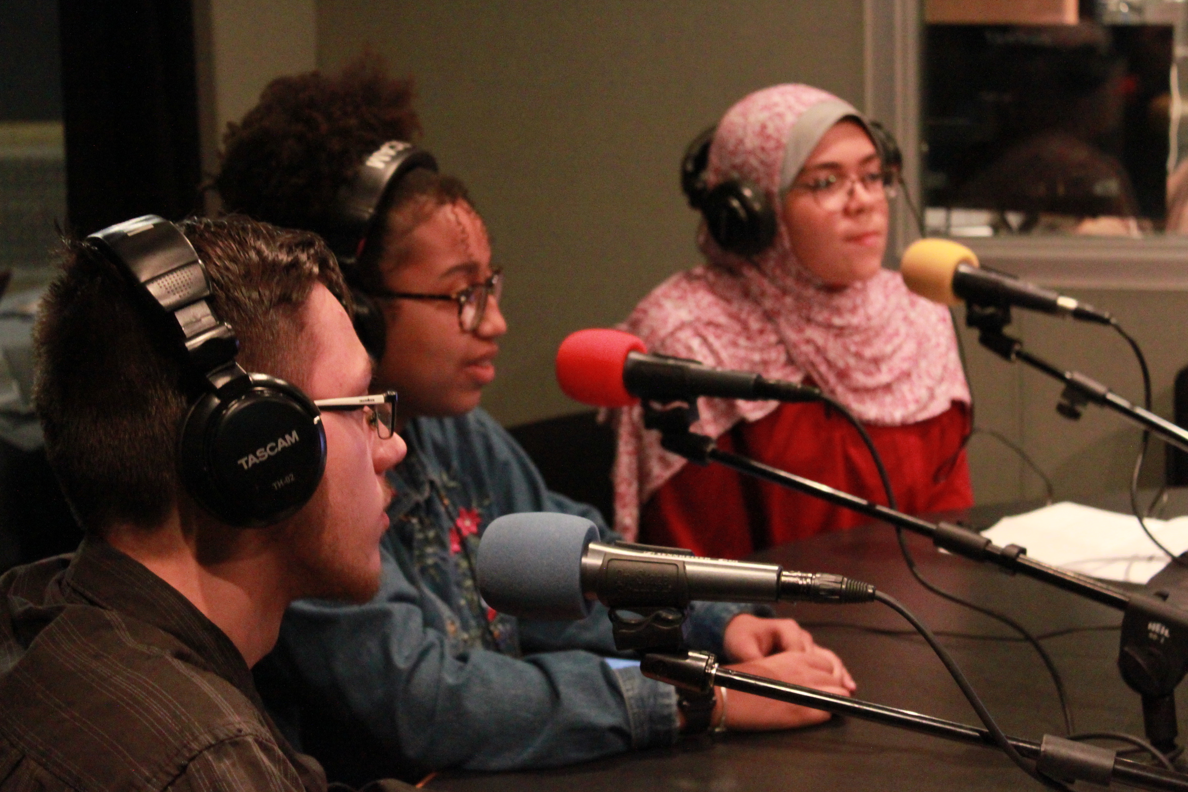 Three teens wearing headphones speaking into microphones in a radio studio