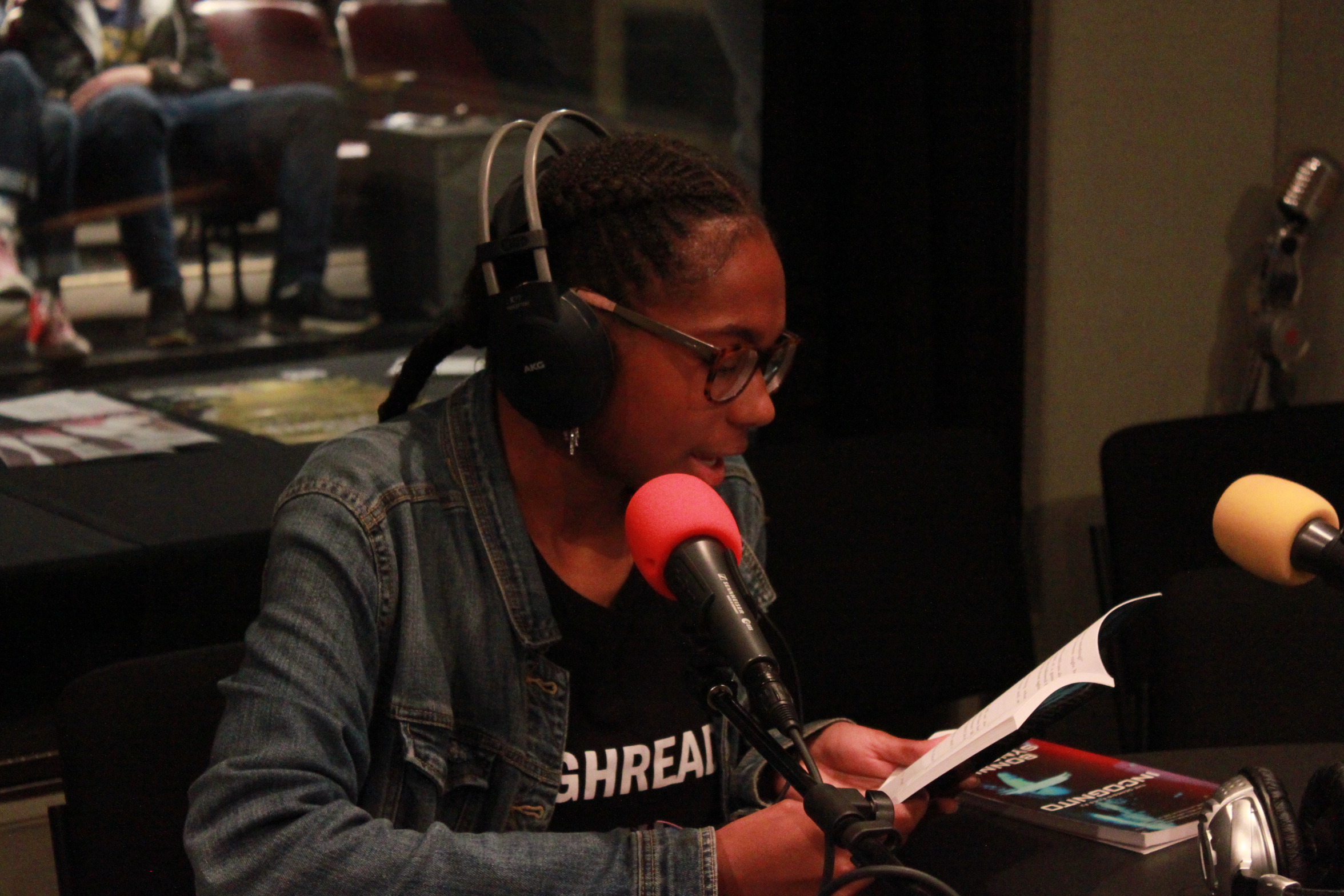 Teen wearing headphones reading from a piece of paper and speaking into a microphone in a radio studio