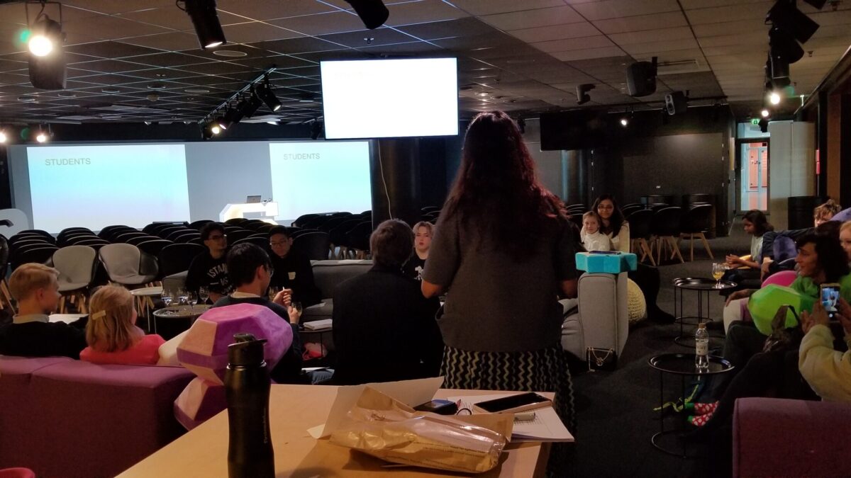 Eighteen young adults sitting while listening and looking at an older adult
