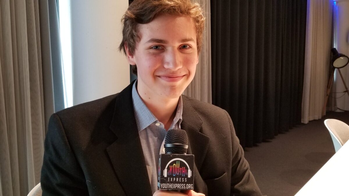 Young adult in a suit jacket holding a microphone and smiling in profile