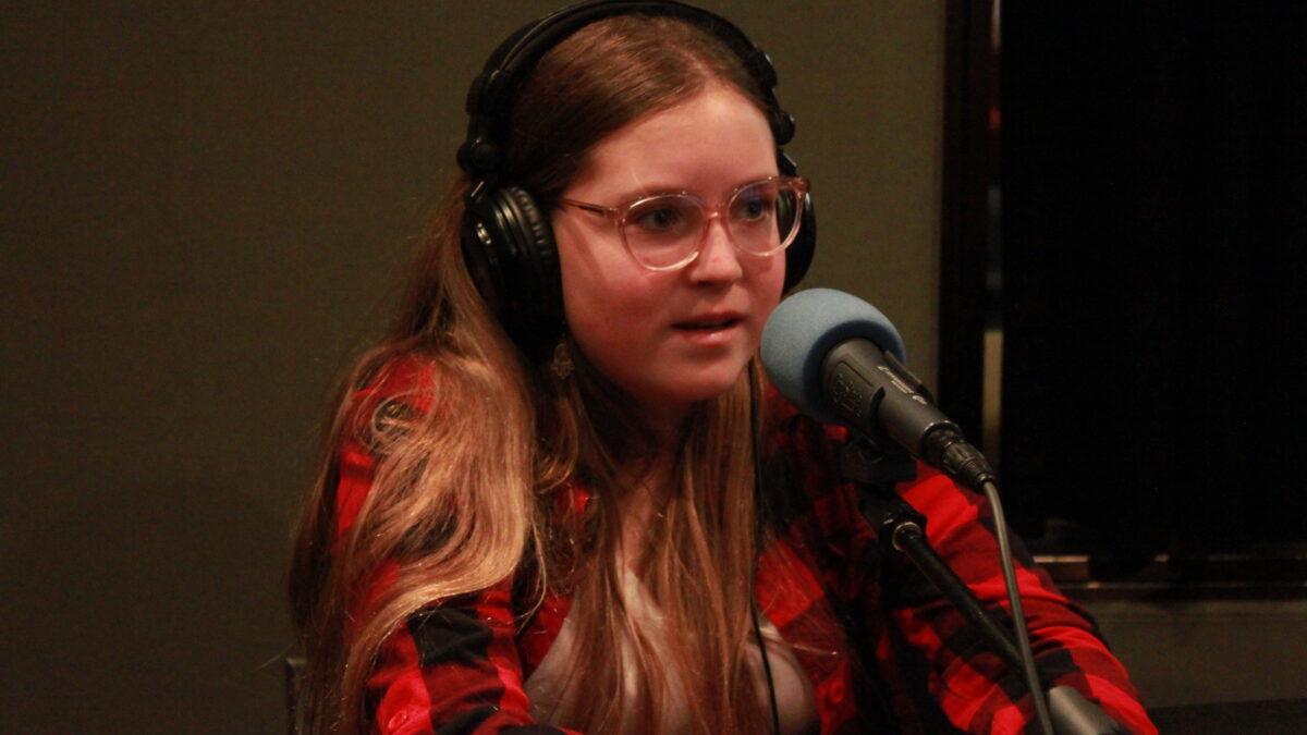 Teen wearing glasses and headphones speaking into a microphone in a radio studio