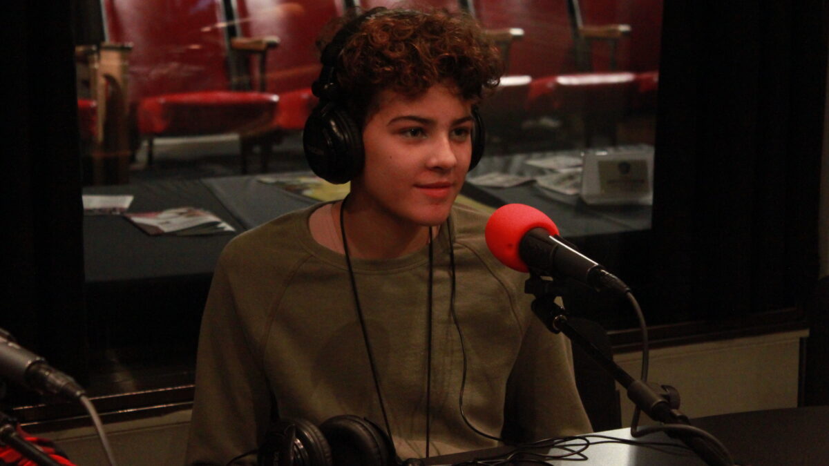 Youth wearing headphones sitting behind a microphone in a radio studio