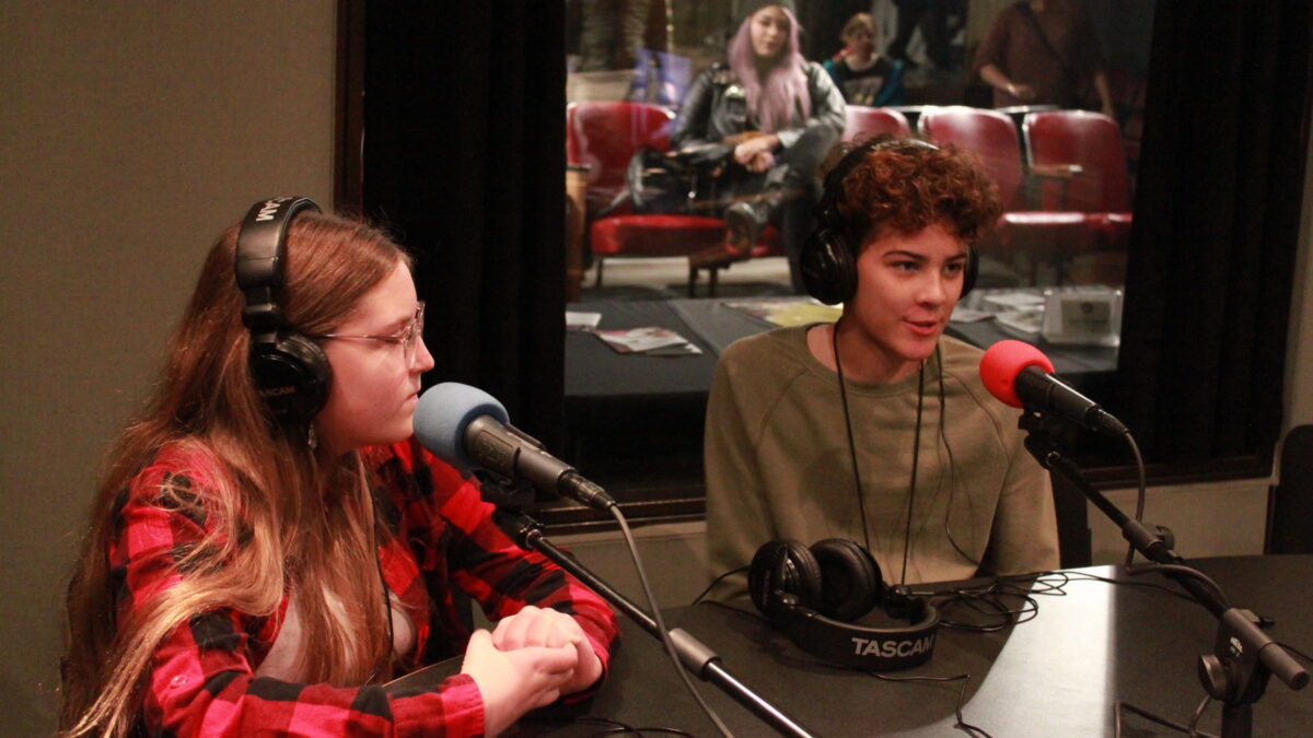 Two youth wearing headphones and speaking into microphones in a radio studio