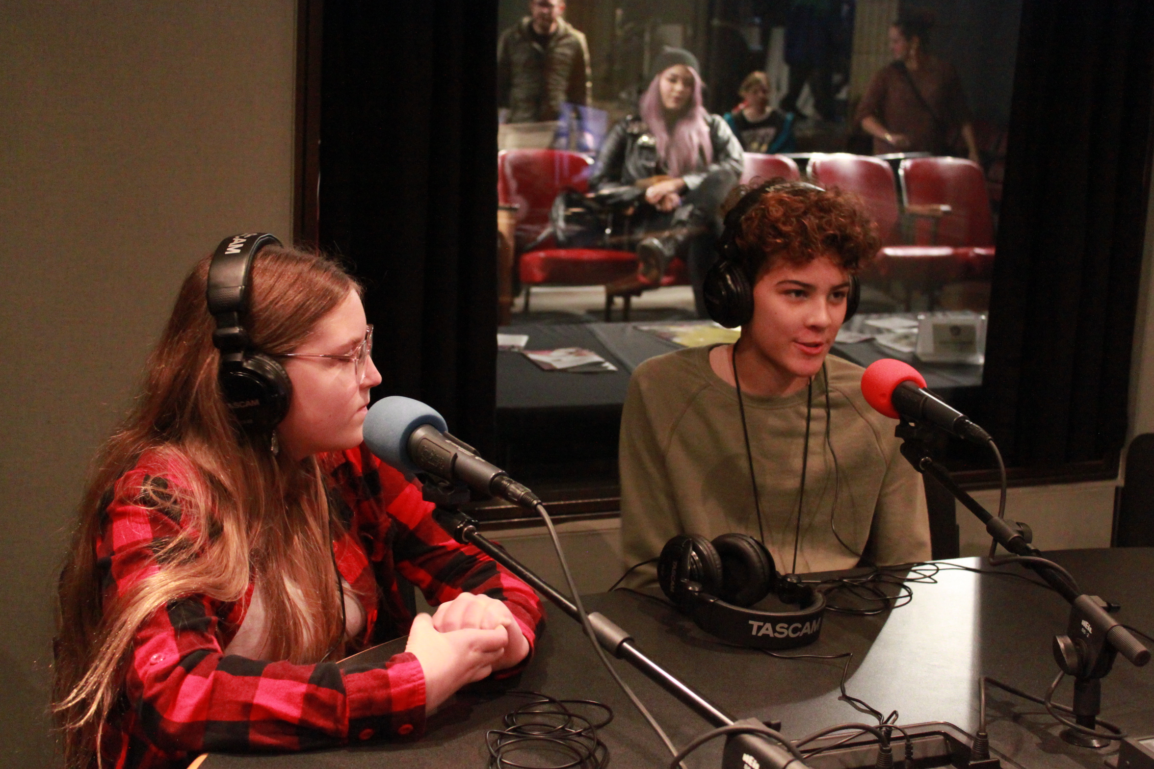 Two youth wearing headphones and speaking into microphones in a radio studio