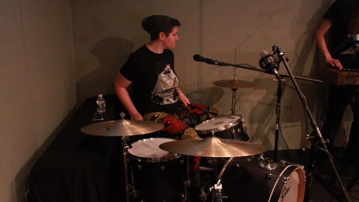 Adult playing on a drum set in front of microphones in a radio studio