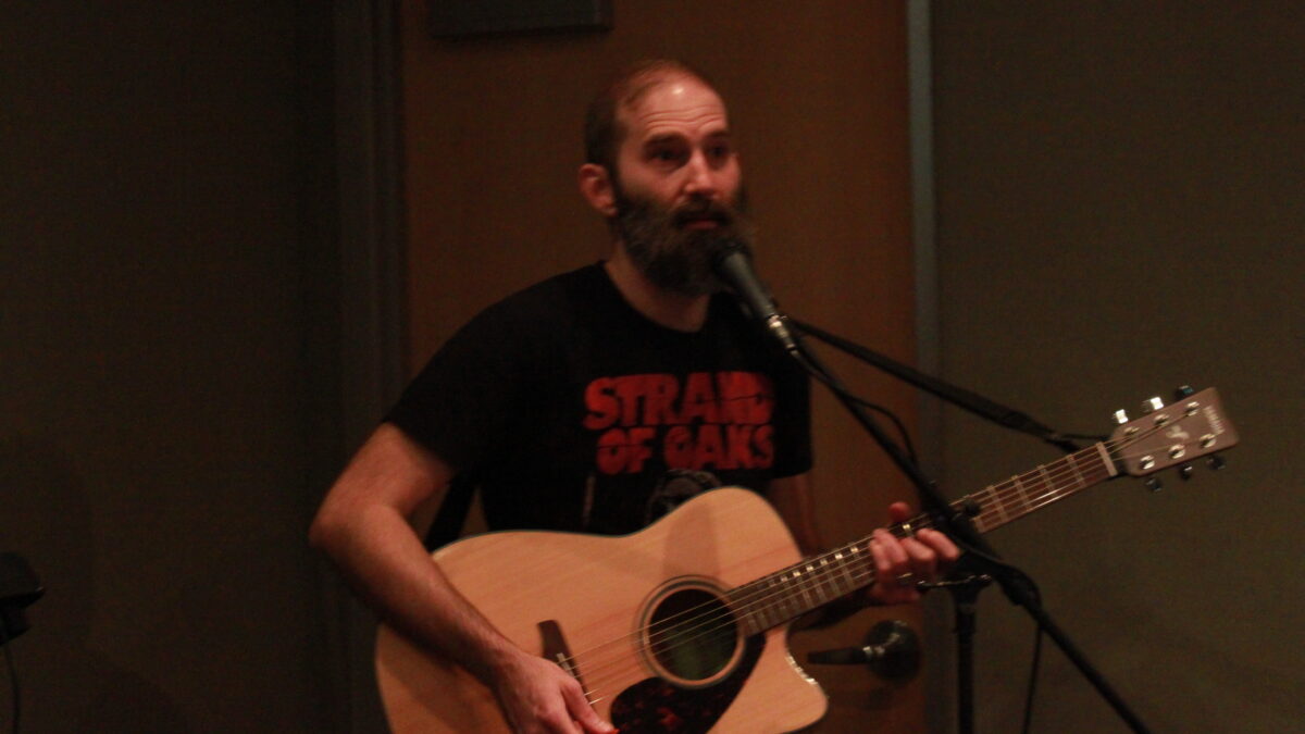 Adult playing guitar and singing into a microphone in a radio studio
