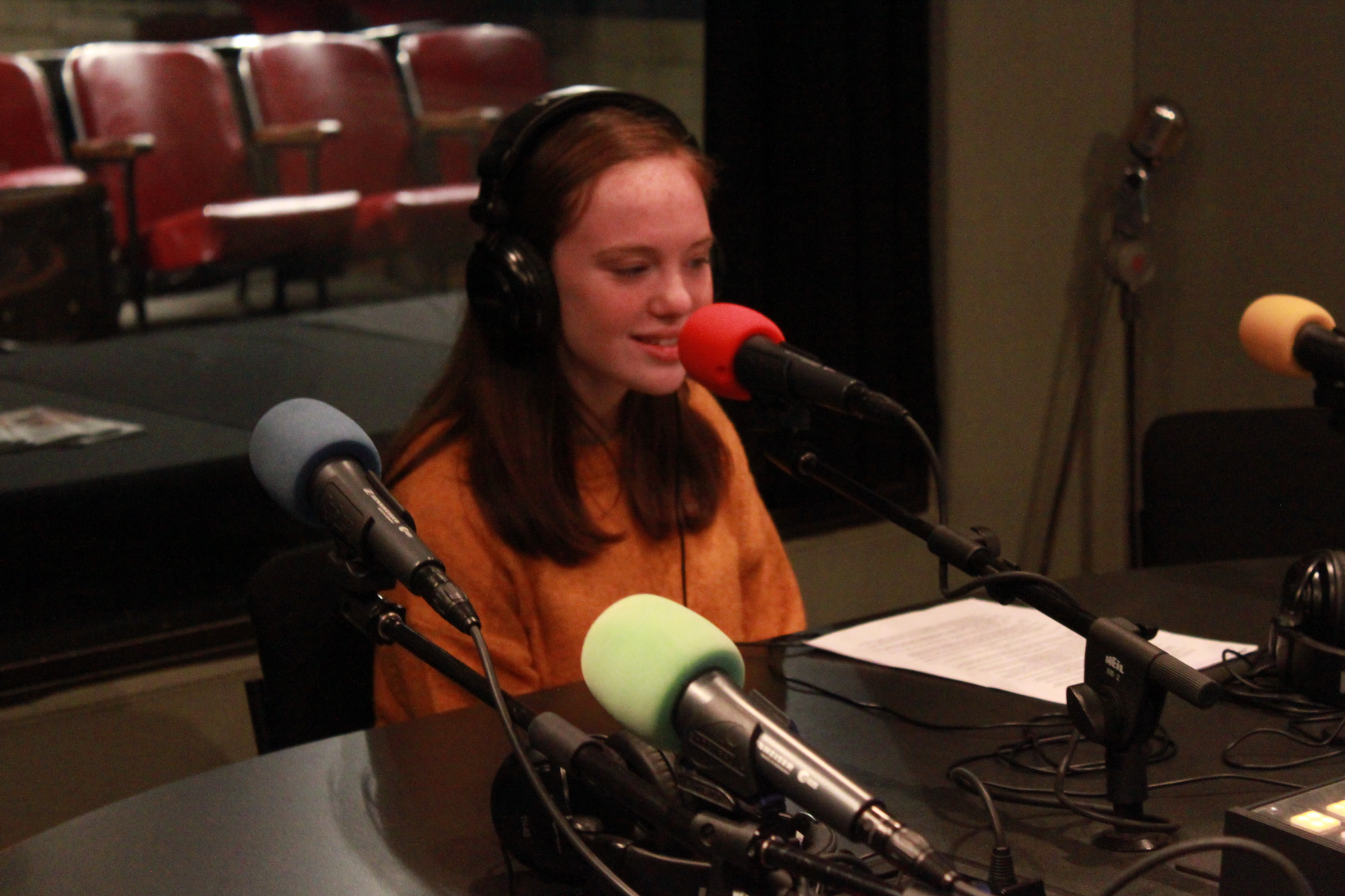 Teen wearing headphones speaking into a microphone in a radio studio