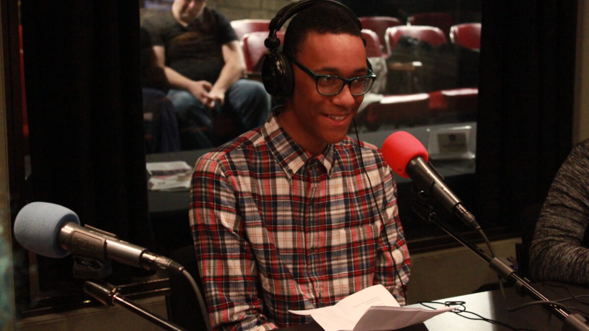 Teen wearing glasses and headphones speaking into a microphone in a radio studio