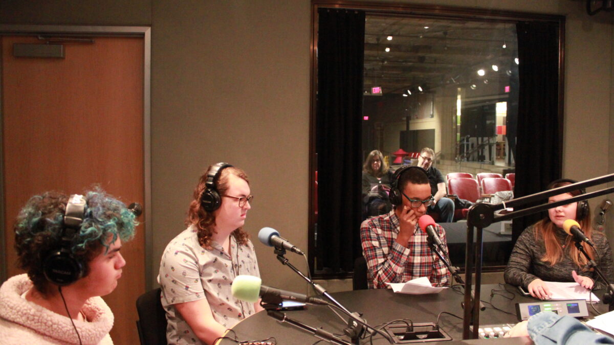Four teens wearing headphones and speaking into microphones in a radio studio