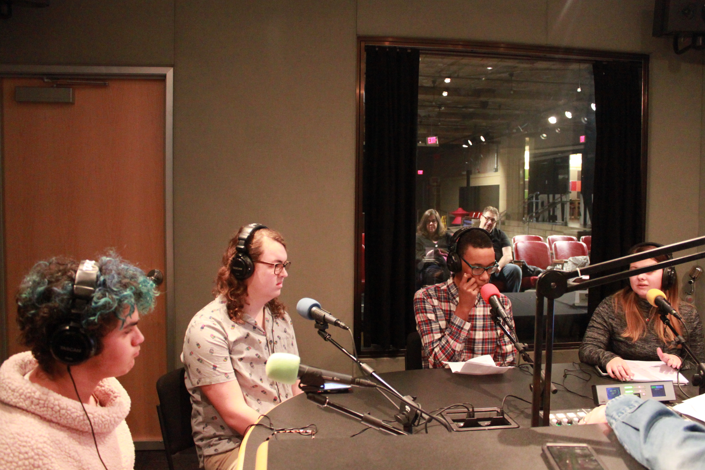 Four teens wearing headphones and speaking into microphones in a radio studio