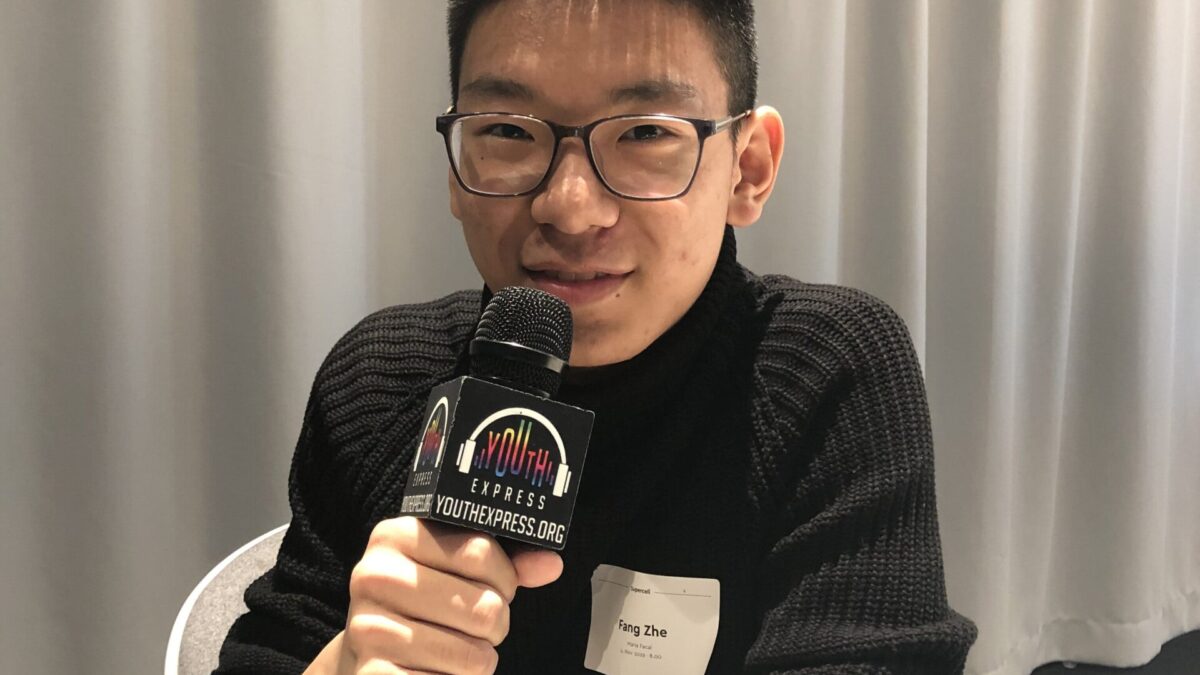 Adult wearing glasses and holding a microphone smiling and posing in profile