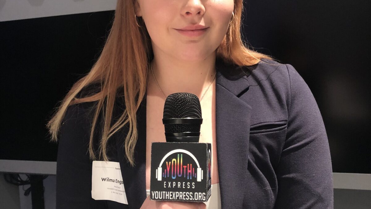 Adult in a suit jacket holding a microphone and smiling in profile